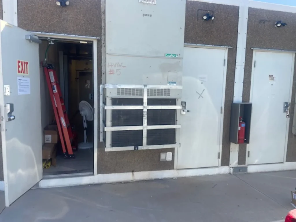 Galvanized flat bar cage installed over a wall-mounted HVAC unit at a commercial building